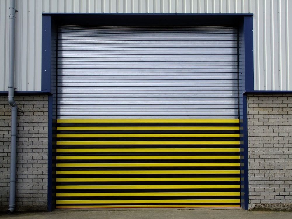 Multicoloured shutter door on warehouse. Top half with clear grey metal stripes, the bottom half with black and yellow bumble-bee style stripes